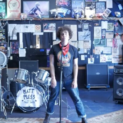 Matt Pless stands in front of a wall covered in ephemera.