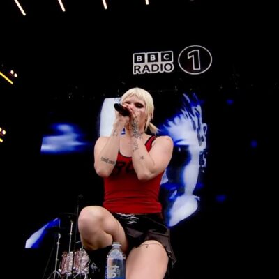 Cassyette kneels on stage at BBC Radio 1's Big Weekend. In the background the band are visible, with a big screen showing Cassyette behind them.