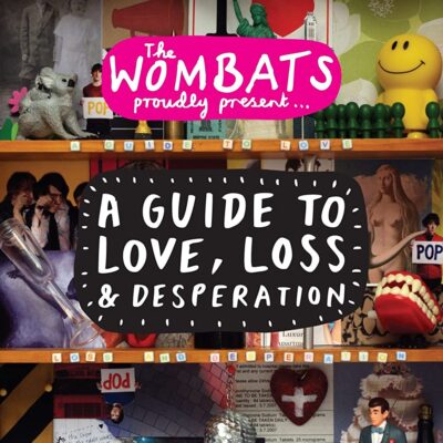 The Wombats. A bookcase with an odd collection of items, like a koala figure, a smile face, a pair of plastic vampire teeth, and photographs.