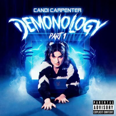 Candi Carpenter - Demonology Part I. Candi climbs out of a TV screen grudge-style, wearing a black and white jumper and with her hair in two high pigtails.