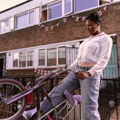 Rachel Chinouriri - It Is What It Is. Rachel stands in front of a terrace with a chopper bike.